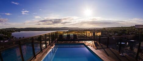Une piscine sur le toit offrant une vue sur un lac et des collines lointaines.
