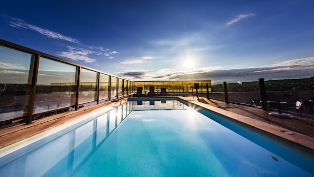 A modern infinity pool with clear glass walls, offering a view of the sunset over a distant landscape. - Lagoon Prime Hotel (Lagoa Santa)