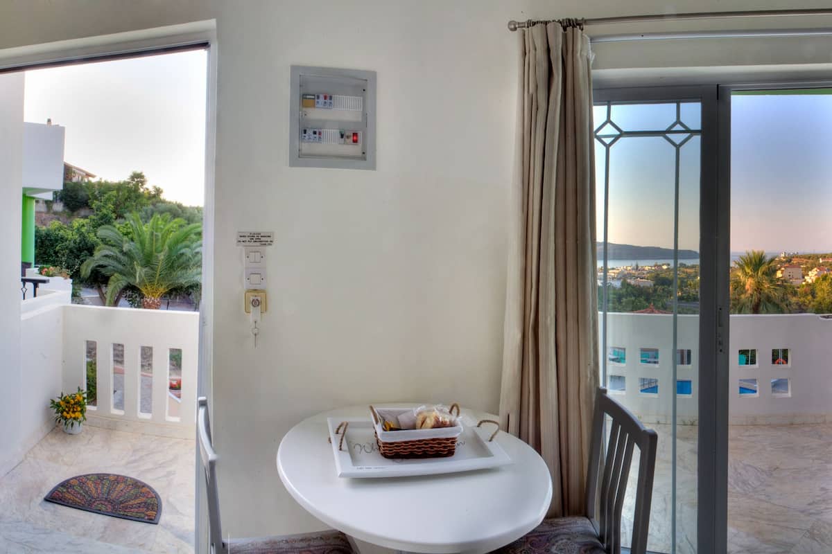 Habitación de hotel con cama, puerta que da a un balcón, una mesita con una cesta y vistas al exterior.