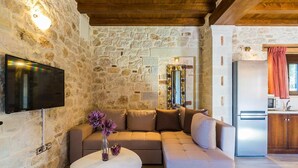 A cozy living area with a stone wall, a flat-screen TV, a beige sofa, and a small round table with a vase. - Villa Life (Chania)