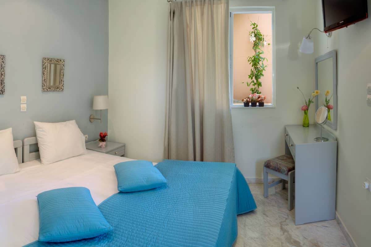 Un dormitorio con una cama, dos mesitas de noche, un tocador, un escritorio con silla, una ventana con cortinas y un espejo.