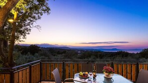 A wooden deck with a glass table set for dining, overlooking a mountainous landscape. - Villa Life (Chania)