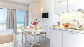 A modern kitchen with white cabinets, a dining area with a white table and wicker chairs, and a view of the sea through large windows. - Aqua Marine (Kissamos)