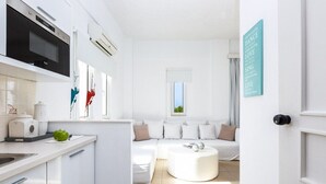 A modern, white-themed living space with a kitchen, a sofa, and a round coffee table. - Aqua Marine (Kissamos)
