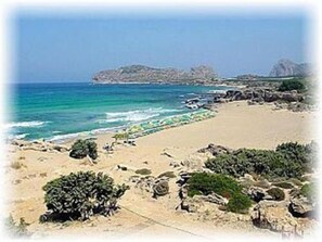 A beach with clear blue water, rocky outcrops, and sparse vegetation. - Aqua Marine (Kissamos)