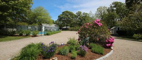 A landscaped garden with a gravel path, flowering plants, and a fenced area with a pool.
