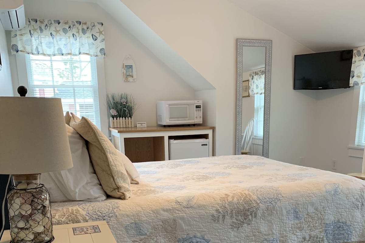 Ein Schlafzimmer mit einem Bett, einem Nachttisch, einer Lampe, einem kleinen Tisch mit einer Mikrowelle, einem Schminktisch und einem Fernseher.