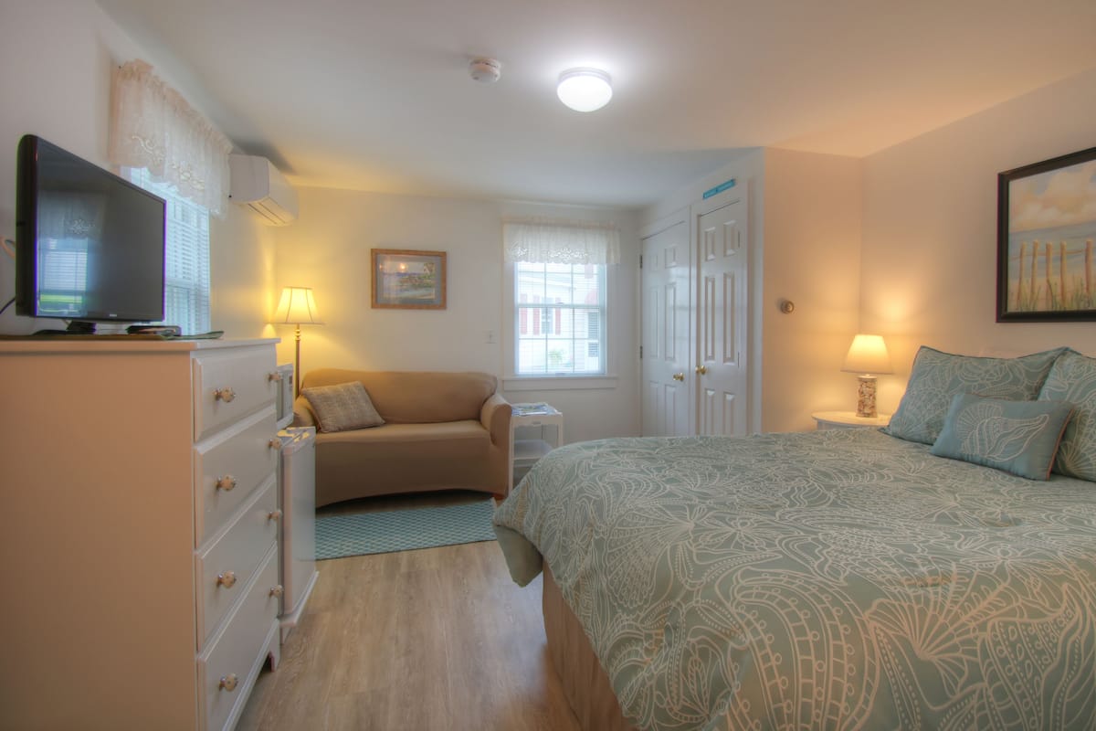 Ein Schlafzimmer mit Bett, Fernseher, Schreibtisch, Stuhl und Fenster.