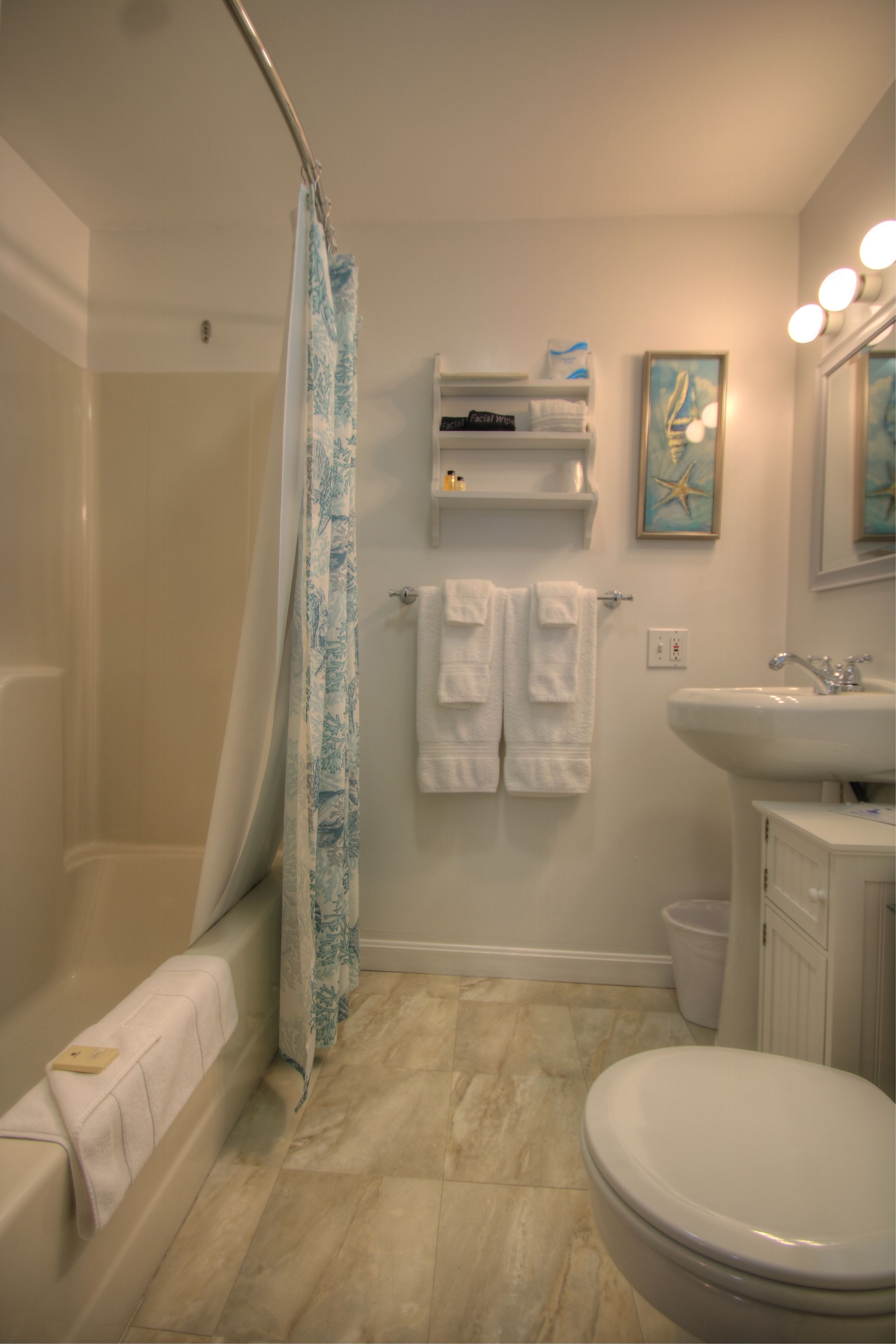 A bathroom with a bathtub, shower curtain, sink, and toilet. There are towels hanging on the wall and a shelf above the sink.
