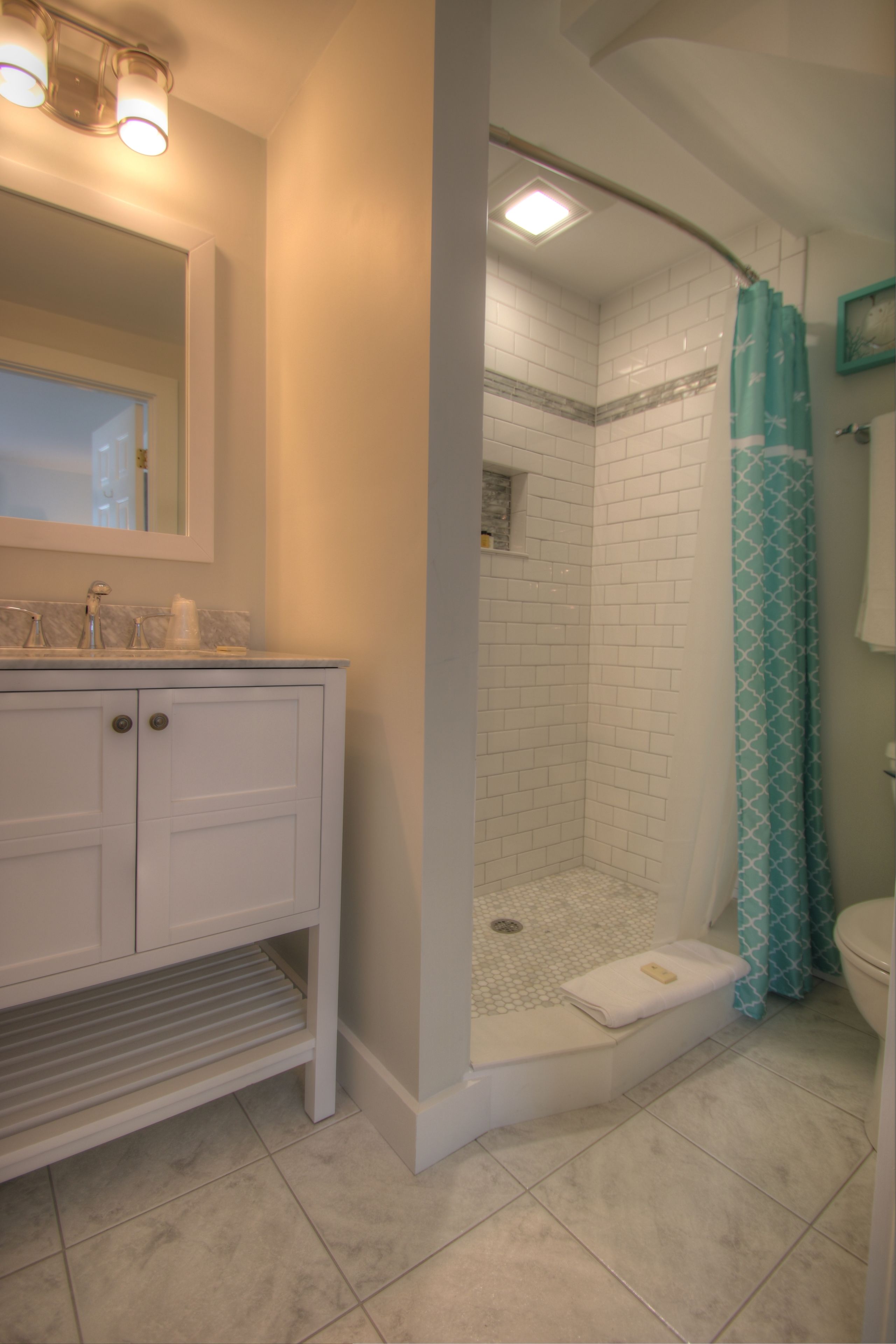 Une salle de bain avec un meuble-lavabo blanc, une douche avec un rideau de douche bleu et des toilettes.