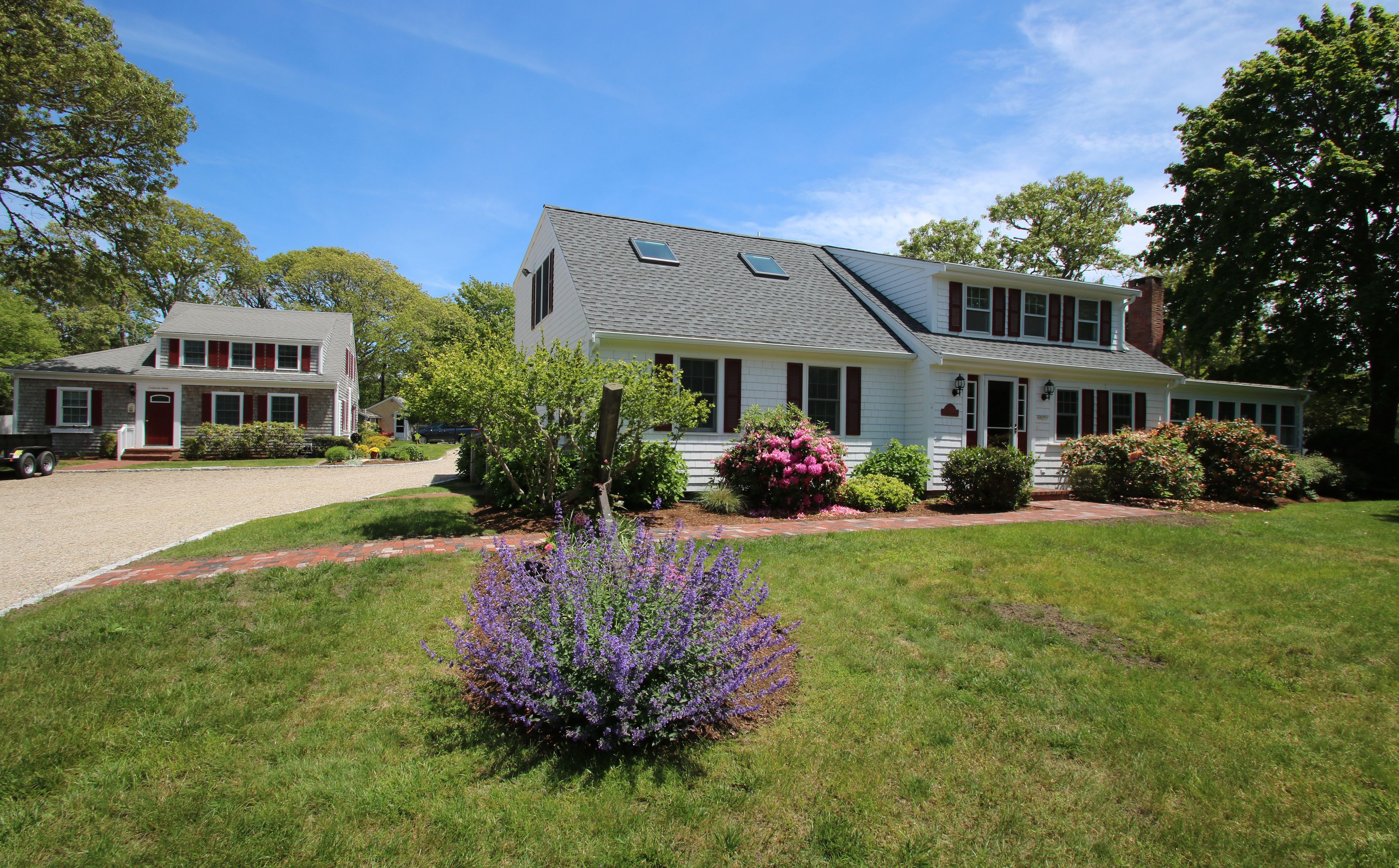 A two-story house with a front porch, a driveway, and a well-maintained lawn with purple flowers.