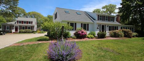 A two-story house with a front porch, a driveway, and a well-maintained lawn with purple flowers.