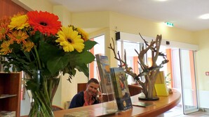 A reception desk with a vase of flowers, a wooden sculpture, and a framed picture. - Hotel Seeblick (Klausdorf)