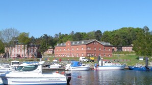 A marina with several boats docked, a large red building with multiple windows, and a clear blue sky. - Hotel Seeblick (Klausdorf)