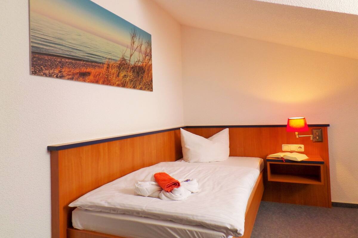 A hotel room with a bed, a nightstand, a lamp, and a painting on the wall.