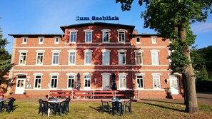 Un bâtiment en briques rouges sur lequel on peut lire l’inscription « Zum Seeblick », avec une terrasse aménagée avec des tables et des chaises.