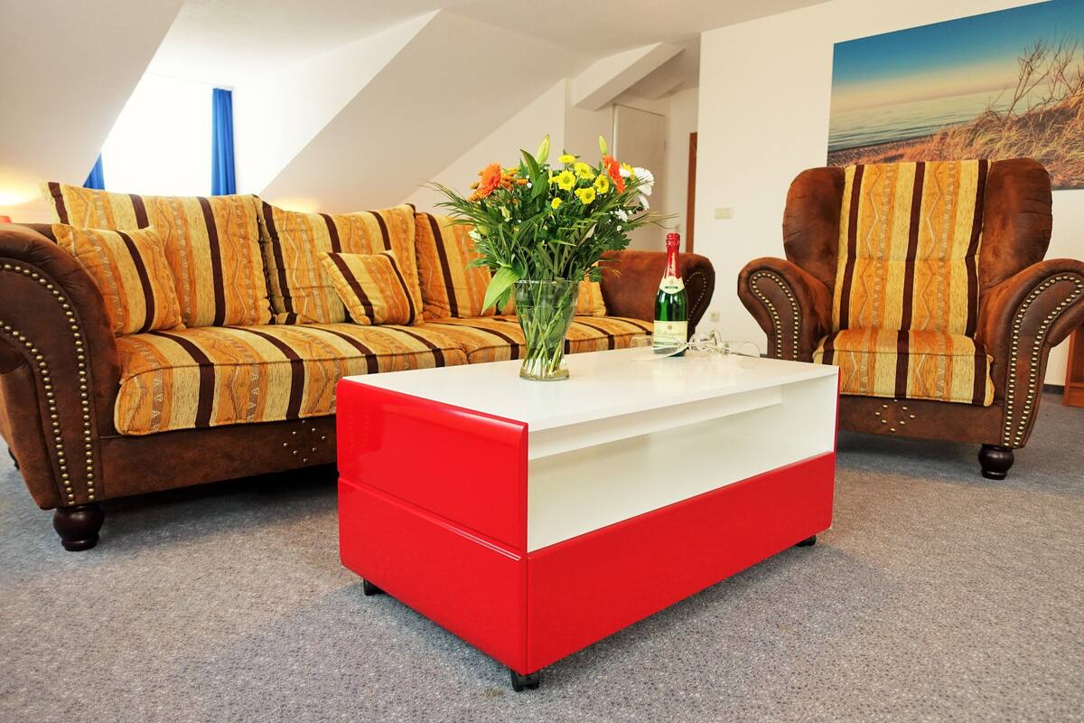 A living room with a brown sofa, a red and white coffee table, and two armchairs.