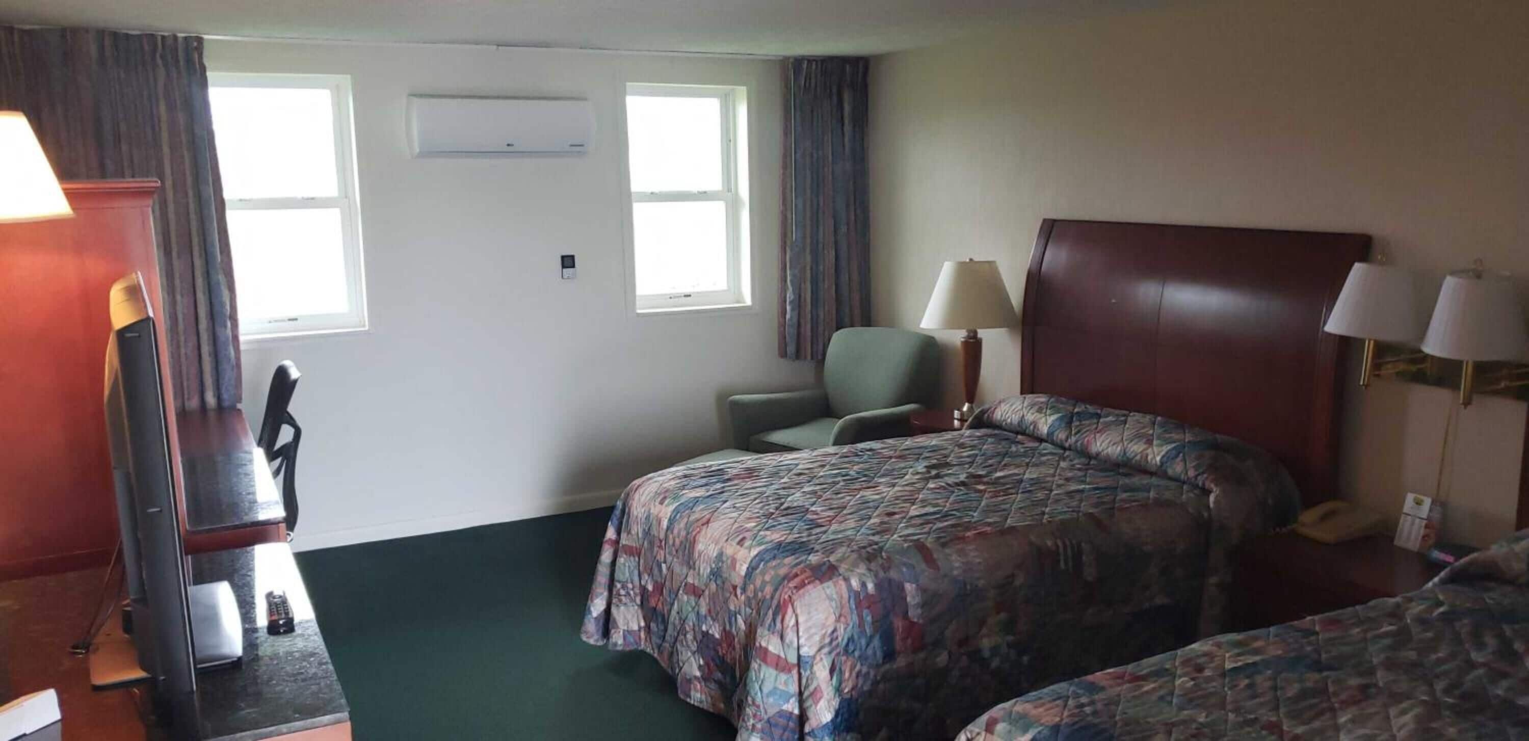 Une chambre d’hôtel avec deux lits, un bureau, une chaise, une lampe et un appareil de climatisation.