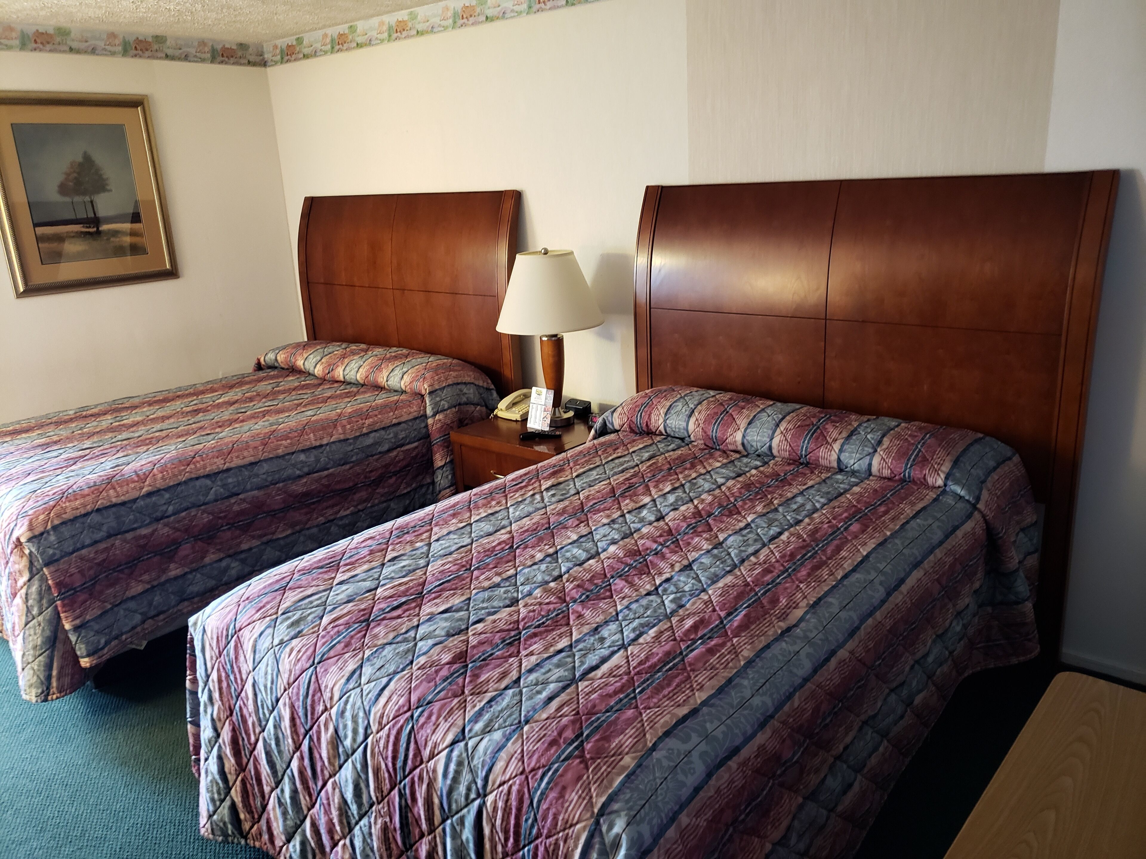 A hotel room with two beds, a nightstand, a lamp, and a framed picture on the wall.