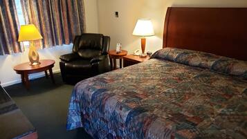 A hotel room with a large bed, a leather chair, two bedside tables with lamps, a telephone, and an air conditioning unit on the wall.