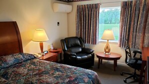 A hotel room with a large bed, a leather chair, a desk with a lamp, and a view of the outdoors. - Huntingdon Motor Inn (Huntingdon)