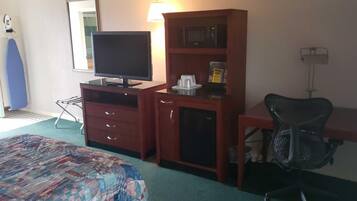 A hotel room with a bed, a desk with a computer, a chair, a television, a microwave, and a small cabinet.