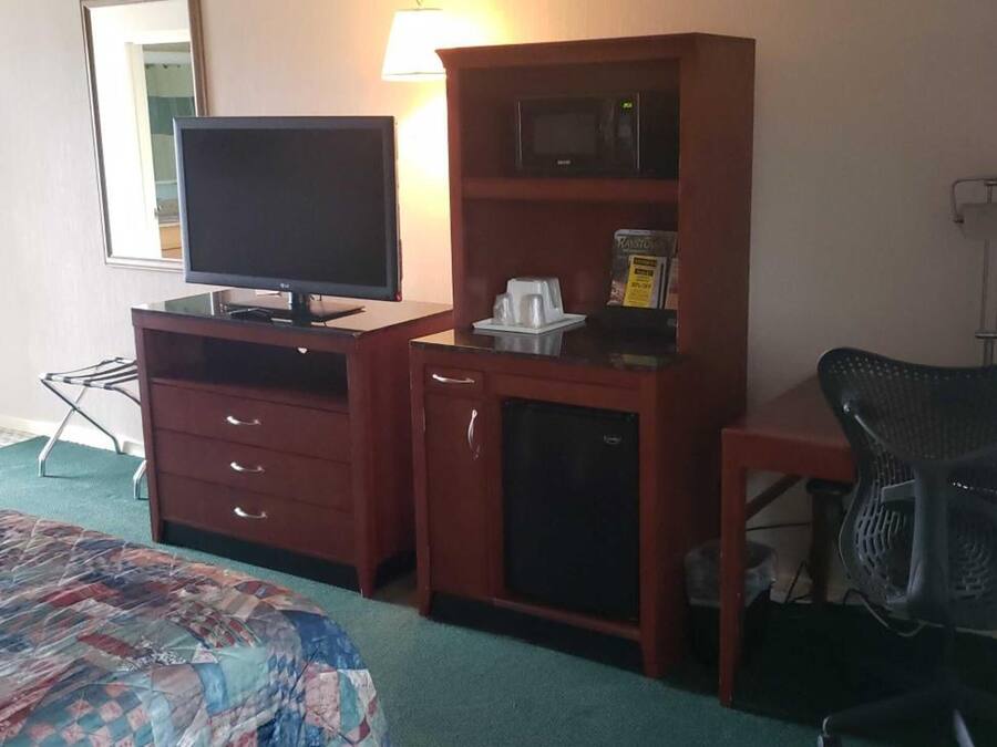 A hotel room with a bed, a desk with a computer, a chair, a television, a microwave, and a small cabinet.
