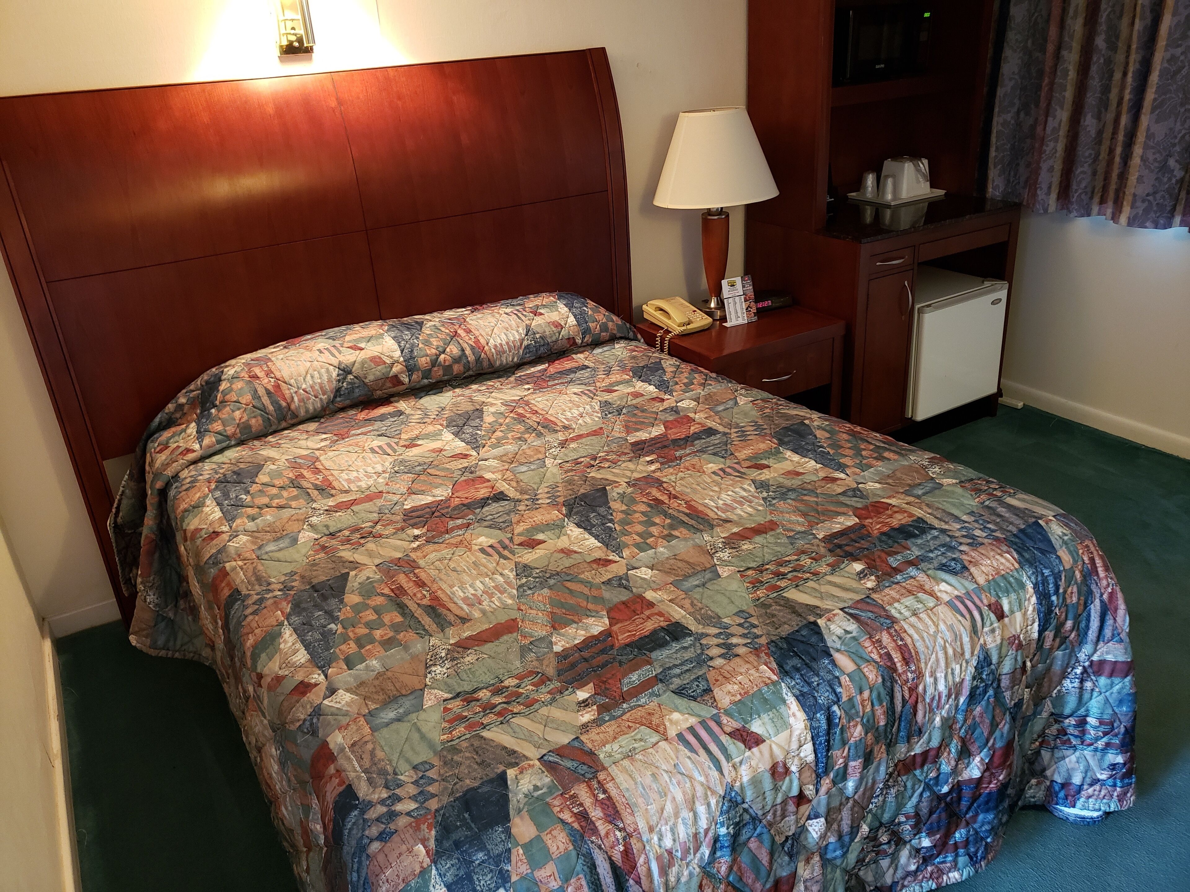 Habitación de hotel con una cama grande, una lámpara de noche, un teléfono y un refrigerador pequeño.
