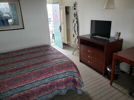 Quarto de hotel com cama, escrivaninha, televisão e guarda-roupa.