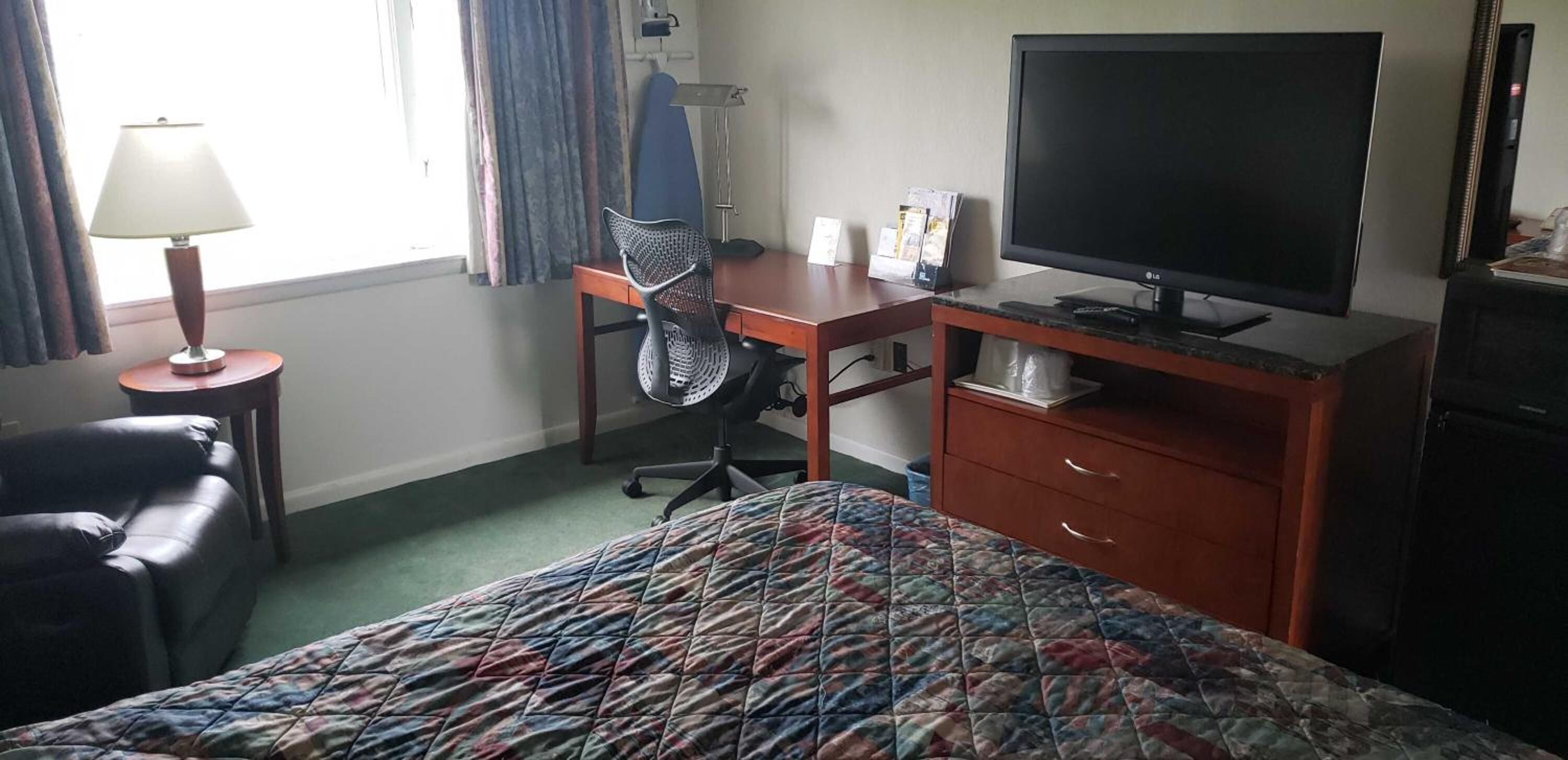 Et hotelværelse med seng, skrivebord, stol, fjernsyn og lampe.
