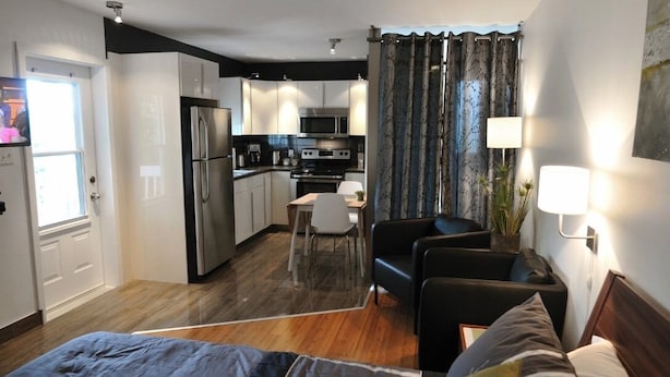 A compact hotel room with a kitchenette, a dining area, and a separate seating area with a bed.