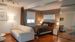 A modern bedroom with a bed, a sofa, a bedside table, a lamp, and a large mirror.