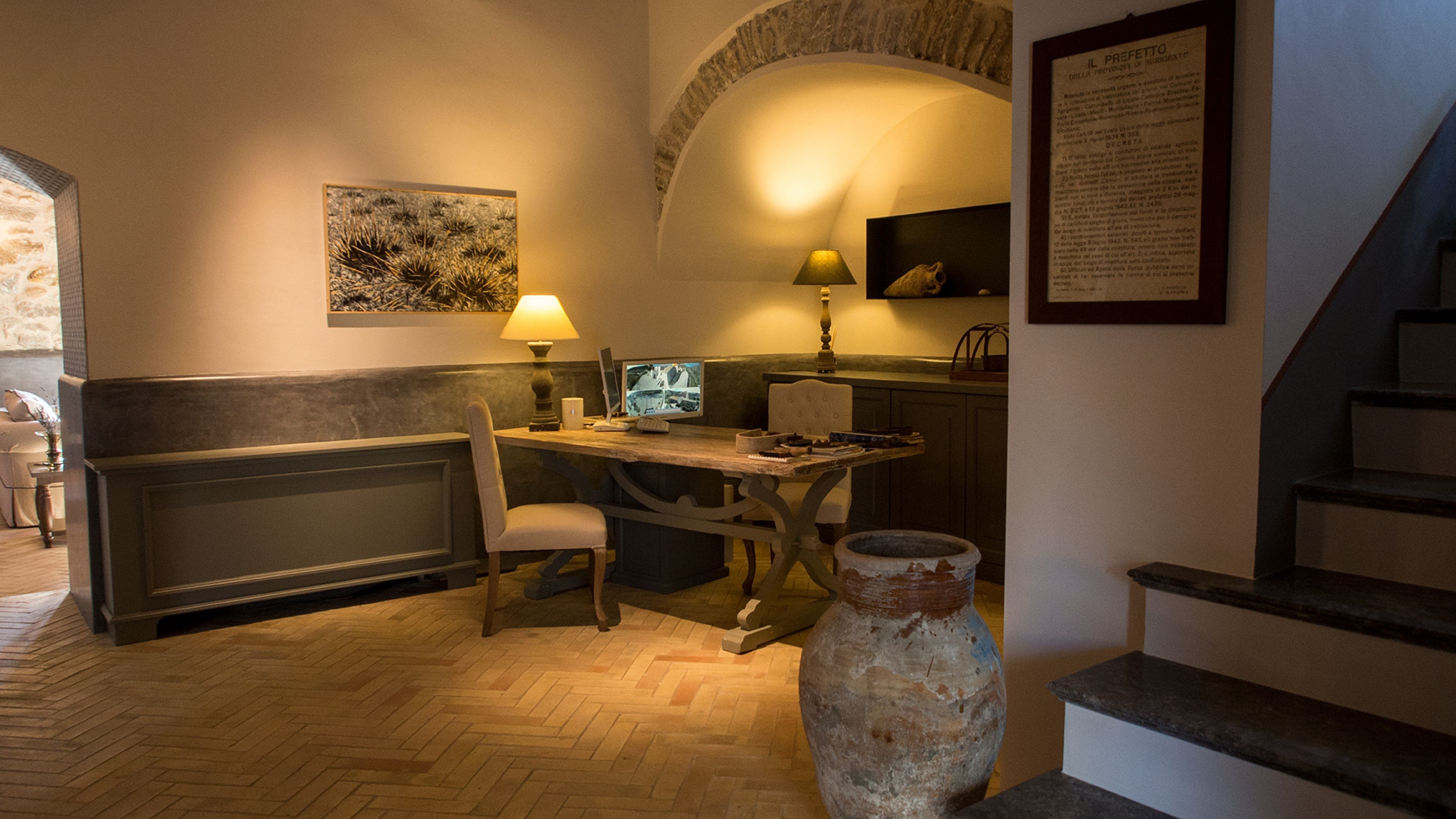 A cozy study room with a wooden desk, a computer, a lamp, and a large vase.
