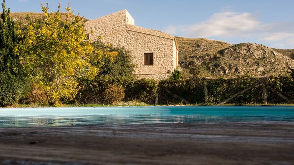 A stone building with a window, surrounded by greenery and hills. - Masseria Agnello Relais (Realmonte)