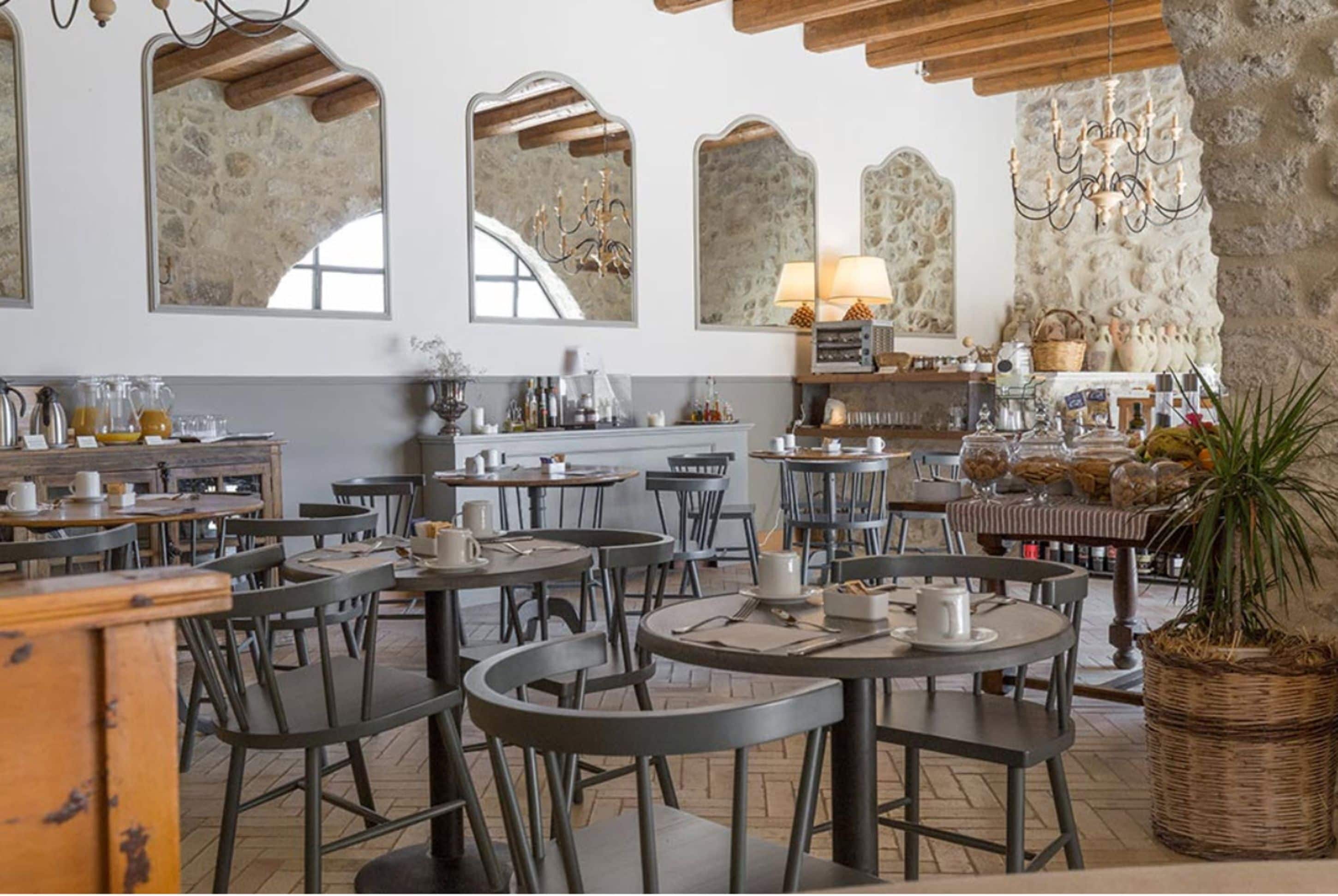 Un café aux murs de pierre rustiques, aux poutres en bois et offrant différents types de sièges, notamment des tables et des chaises.