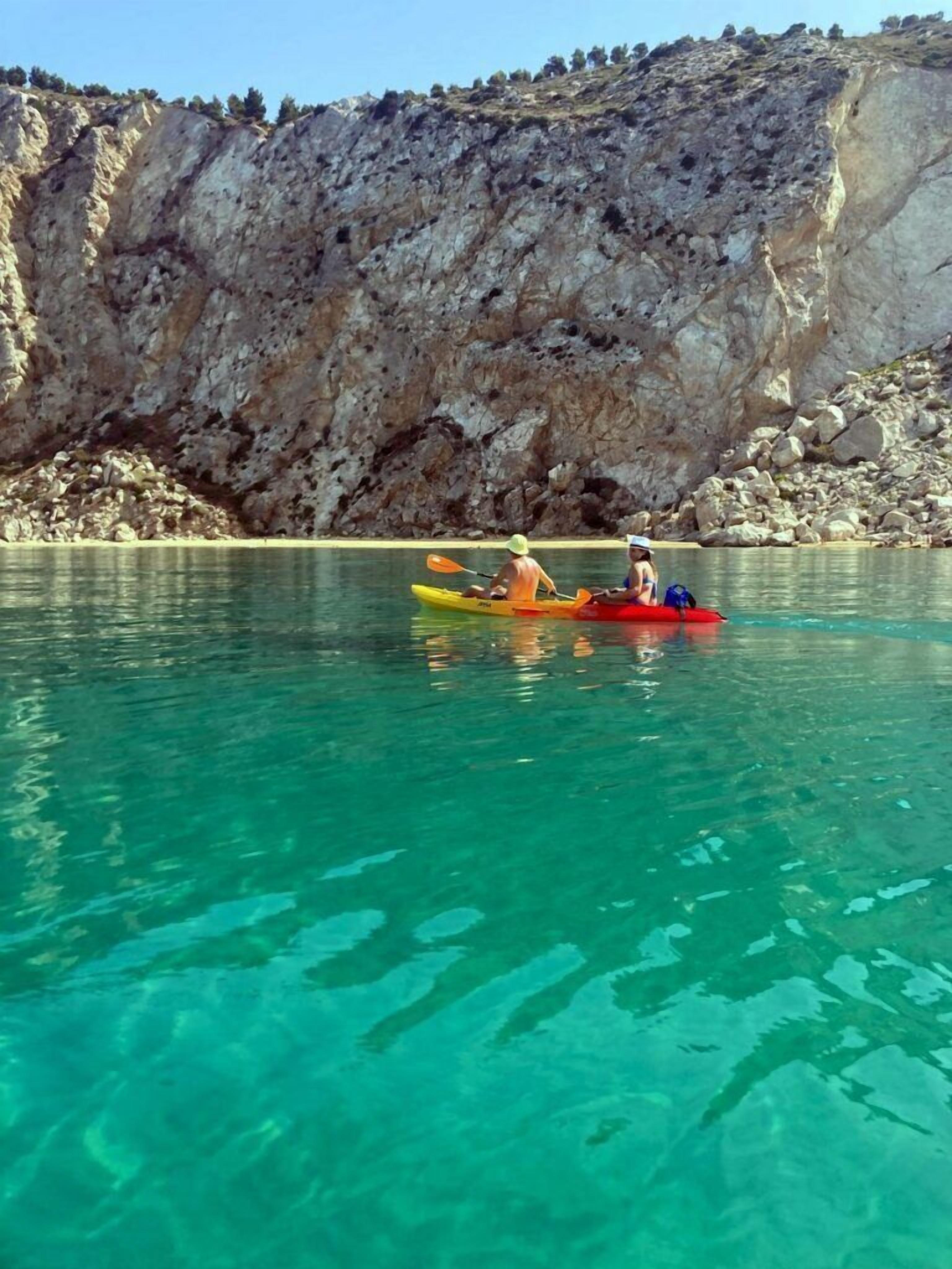 Kayakistas en un lago tranquilo y cristalino, con acantilados rocosos al fondo.