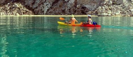 Kayakers on a calm, clear lake with rocky cliffs in the background.