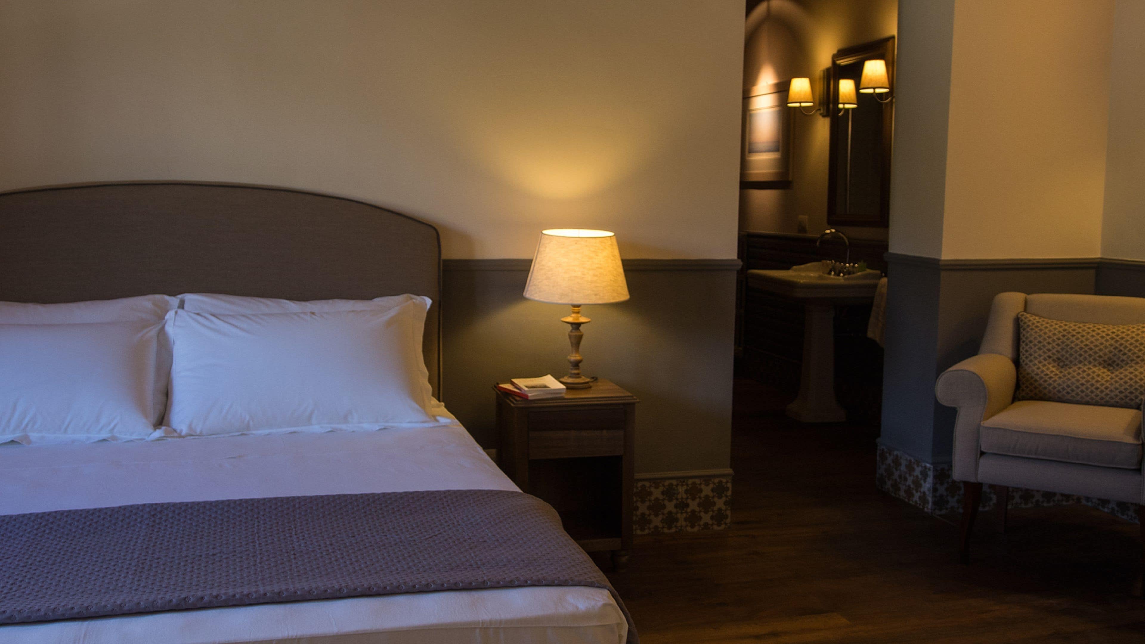 Une chambre d’hôtel avec un lit, une lampe de chevet, une chaise, un lavabo et un miroir.