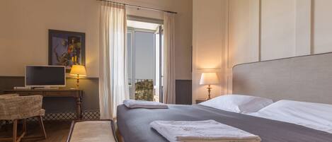 A hotel room with a large bed, a desk with a computer, a chair, and a window with curtains.