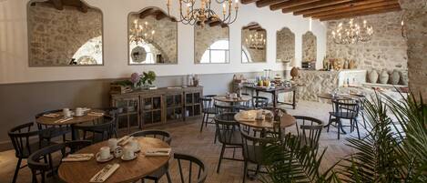 A restaurant with wooden tables and chairs, stone walls, and a chandelier.