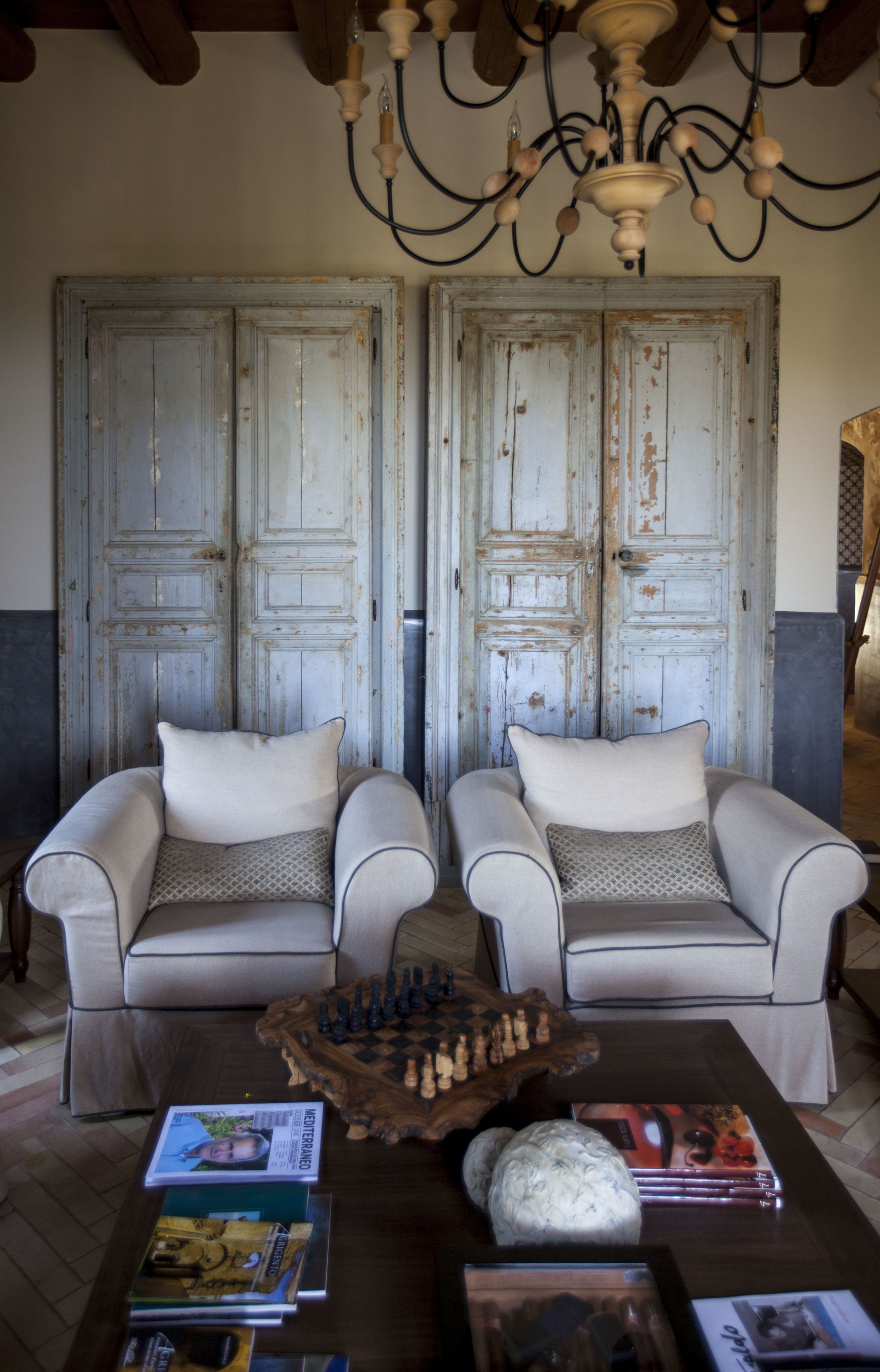 A room with two armchairs, a wooden coffee table with books and a chess set, and a chandelier.