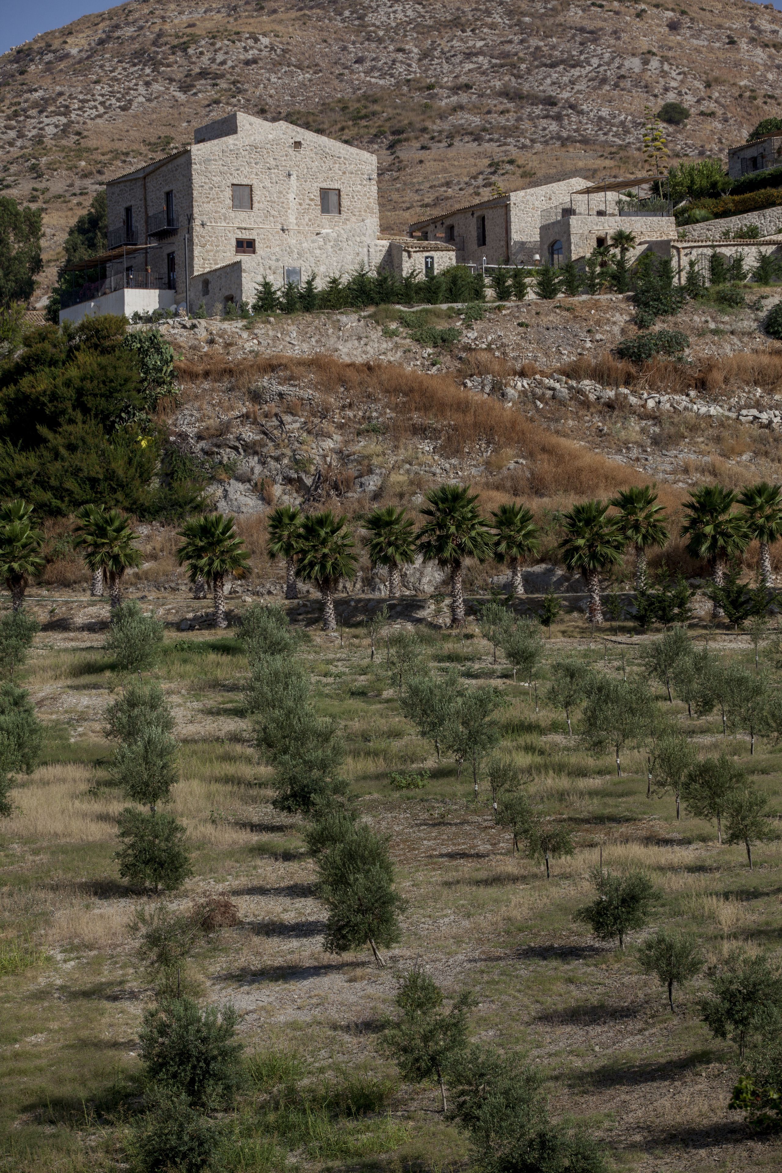 Un edificio de piedra con varias habitaciones, rodeado por un paisaje árido con vegetación escasa y una colina al fondo.
