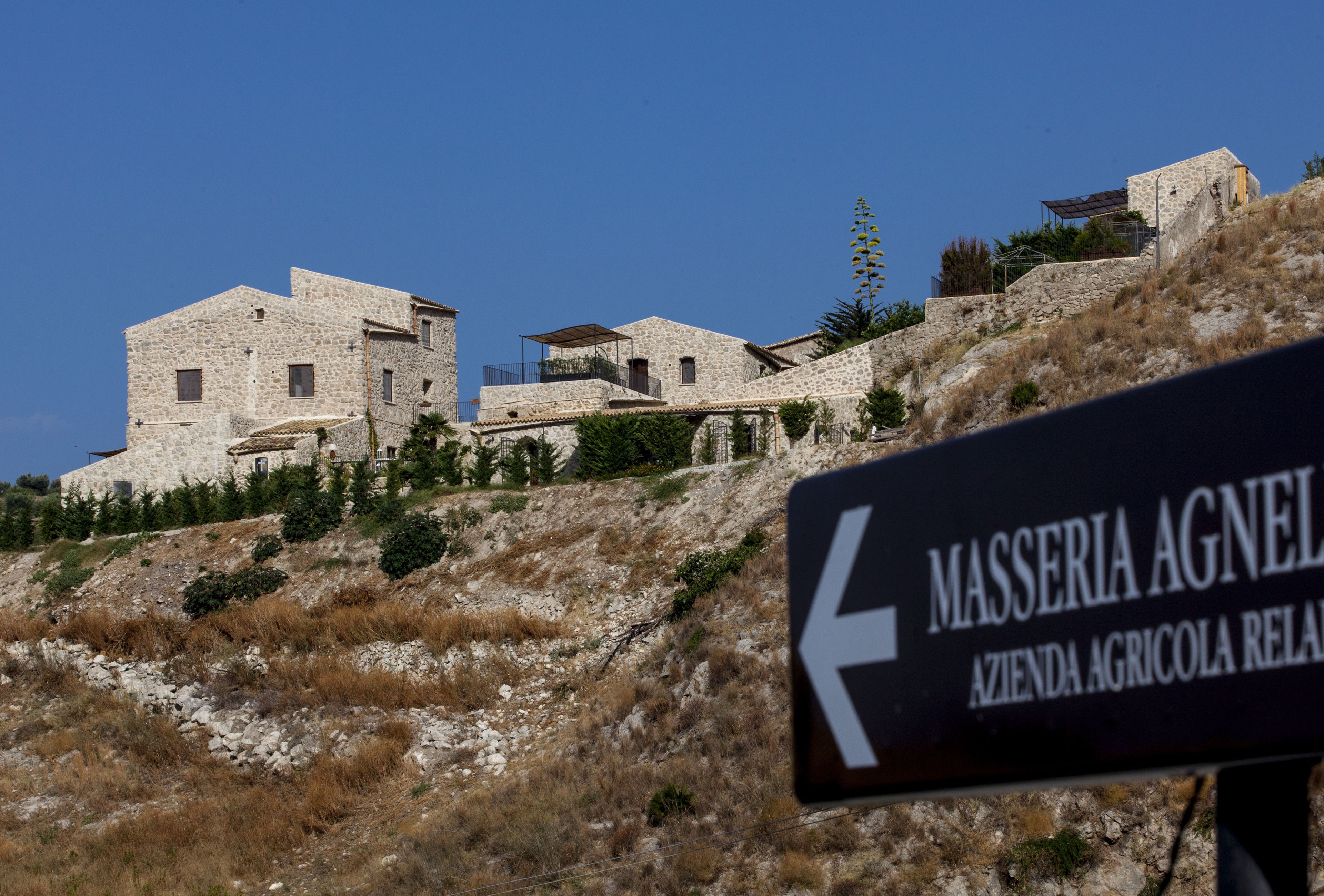 Um edifício de pedra com uma placa indicando 'MASSERIA AGNEL AZIENDA AGRICOLA RELAT'.