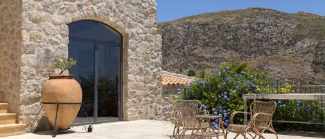 A stone building with a large arched doorway, outdoor wicker furniture, and a view of a hill.