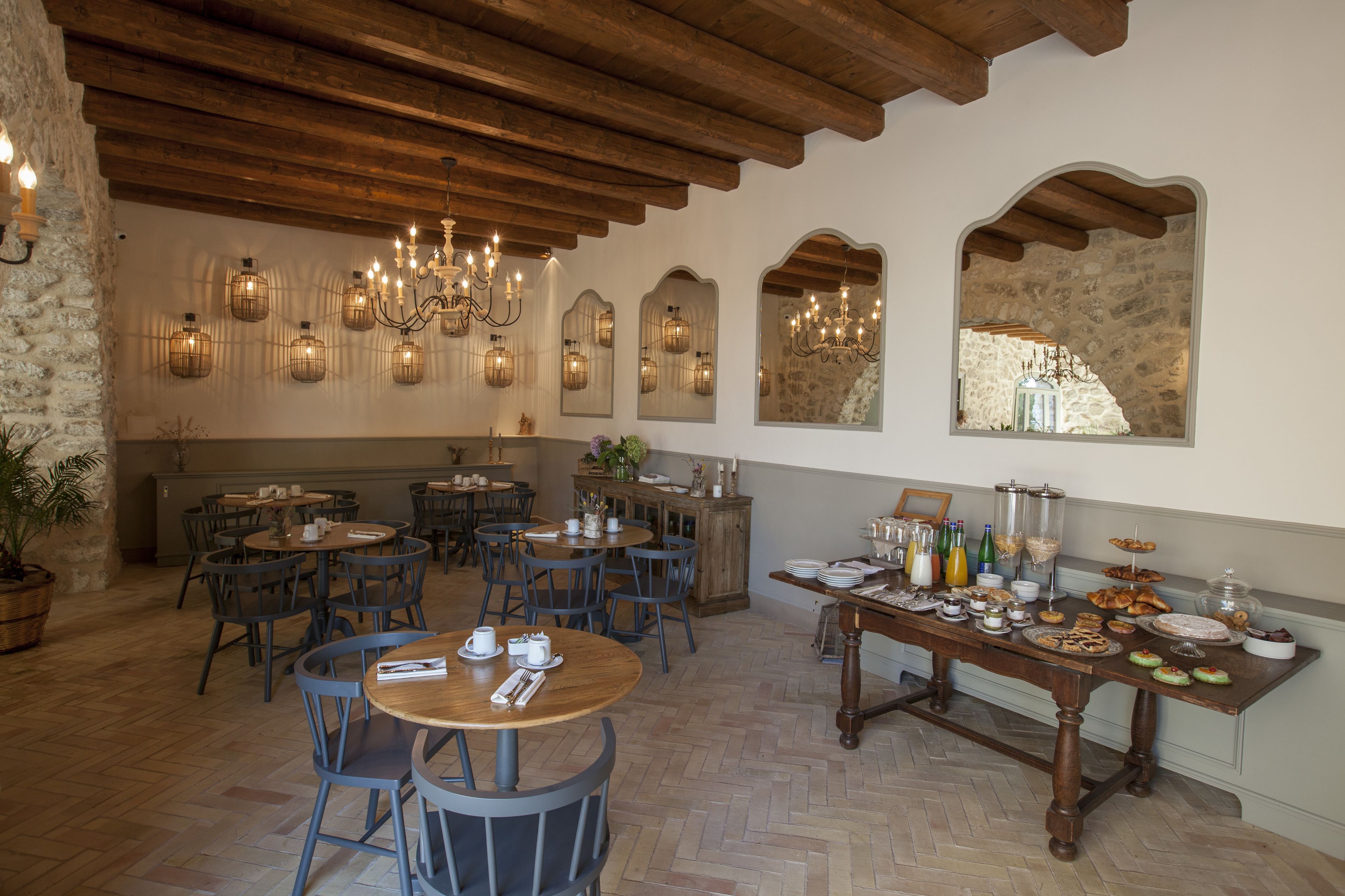 A dining area with wooden tables and chairs, a buffet table with various food items, and a stone wall with arched windows.