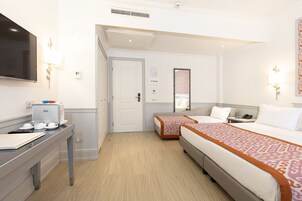Una habitación de hotel con cama, mesita de noche, televisor y escritorio con cafetera.