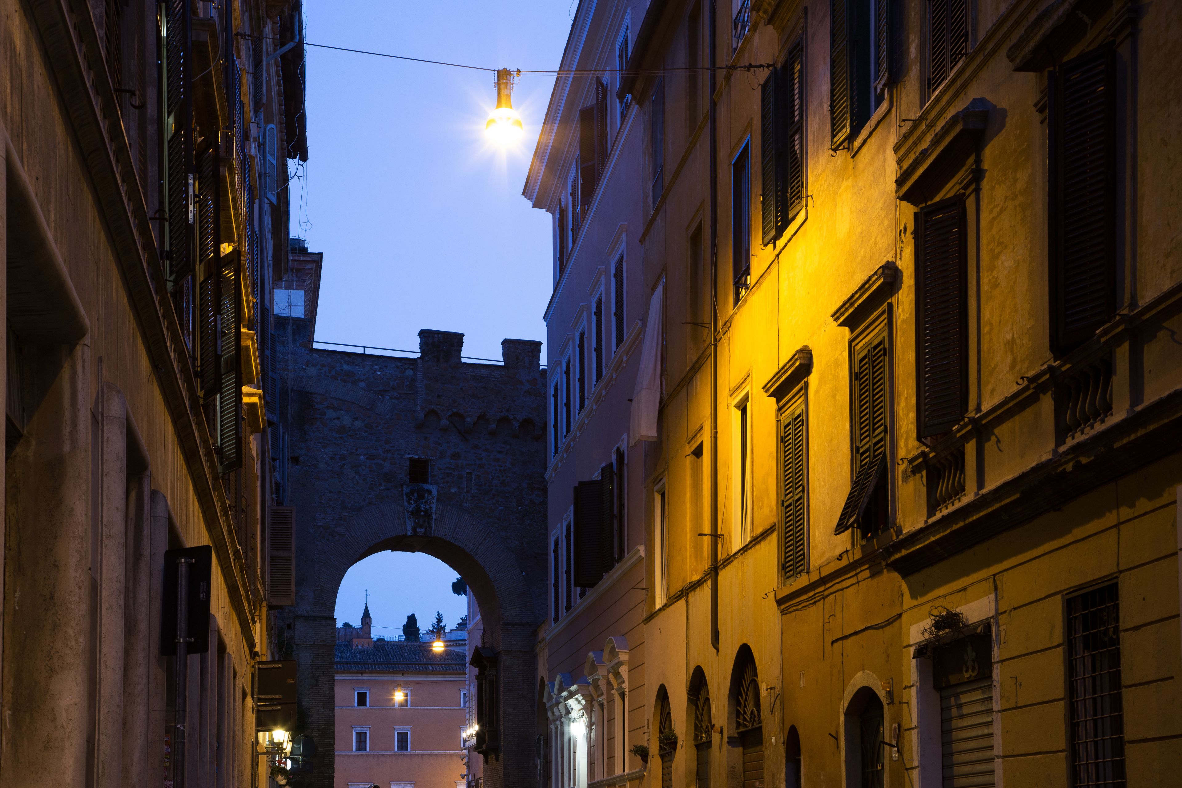 Una calle estrecha flanqueada por edificios, un arco y un farol.