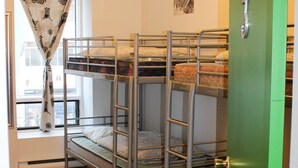 Una habitación con literas, una ventana con cortina, una araña y una puerta verde.