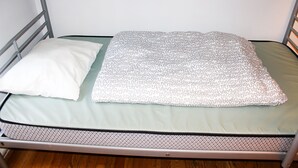 Una cama con estructura de metal, colchón verde y manta estampada.