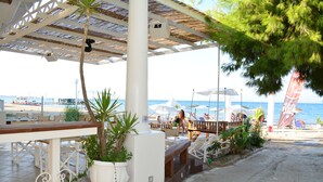 A beachside restaurant with outdoor seating, a view of the sea, and a palm tree. - Cavo D'Oro Apartments (Corfu)